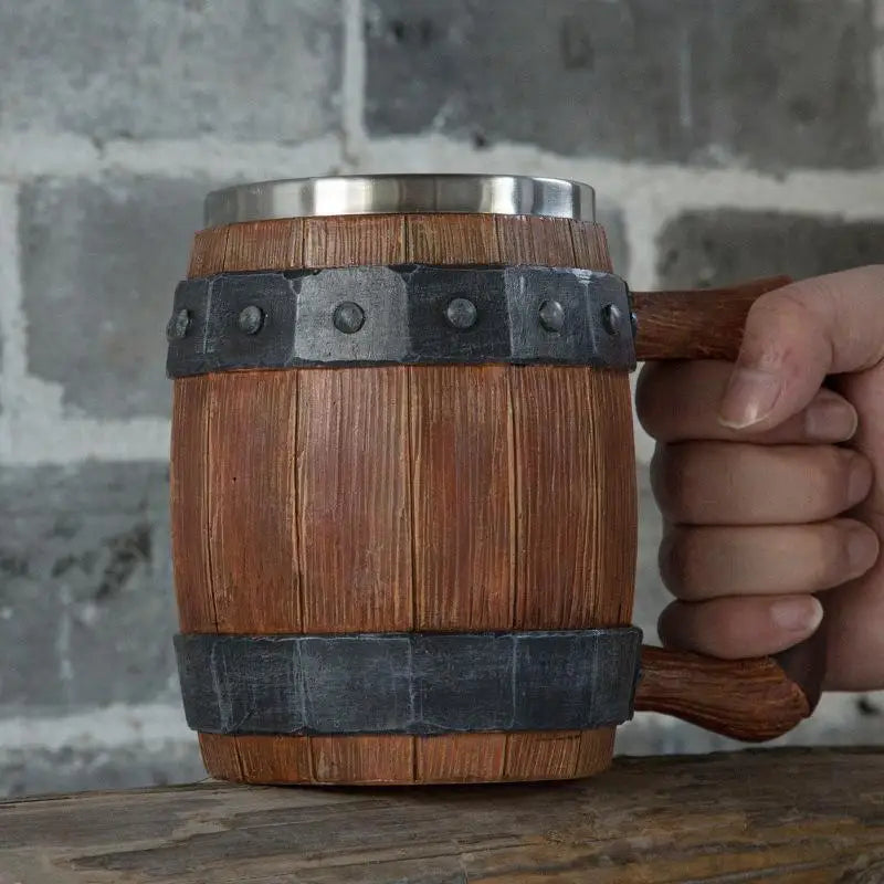 Wooden mug with metal banding held by a hand against a gray brick wall.